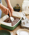Mini stainless steel spatula with black handle scraping brownie batter in a green baking dish