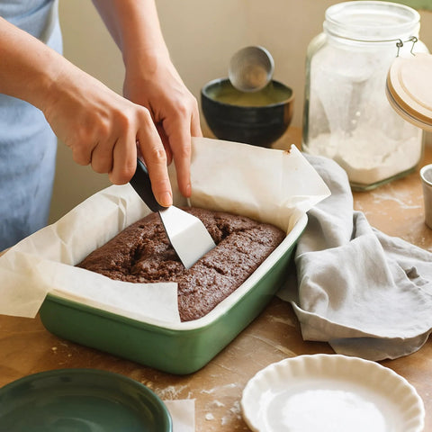 Mini stainless steel spatula with black handle scraping brownie batter in a green baking dish