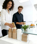 Two people using a clear acrylic coffee cup and lid holder with straw organizer five compartment disposable cup dispenser on counter.