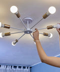 Person installing a light bulb into a modern ceiling fixture with brass accents in home setting.