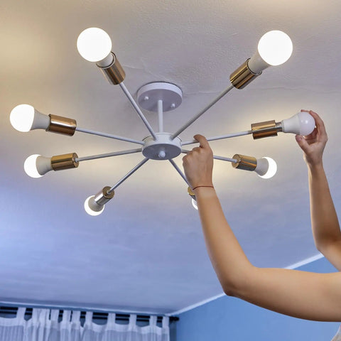Person installing a light bulb into a modern ceiling fixture with brass accents in home setting.