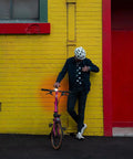 Person leaning on a yellow brick wall with a bicycle equipped with a USB Rechargeable Bike Light With 250 Lumen Front Headlight Ride Ready Low Battery Indicator Side Visibility Cutouts IP67 Waterproof Five Modes And Up To 240 Hours Of Runtime visible on the handlebars.