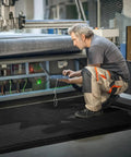 Worker using a laptop while standing on an Anti Fatigue Standing Mat For Industrial Kitchens And Workshops, 2 Ft By 5 Ft, 15/16 Inch Thick Ergonomic Memory Foam Cushioned Floor Mat With Diamond Plate Texture, Heavy Duty Back And Leg Pain Relief For Long Shifts.