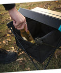 Person placing bottle in storage bag of Foldable Camping Table With Storage Bag Kit For Picnic And Barbecue Quick Assembly Portable Beach Table Tailgate Ready Easy Fold Unfold Durable Plastic Connectors Keeps Gear Neat And Ready For Outdoor Adventures on grass.