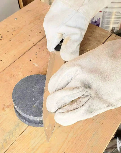 Gloved hand sharpening blade on 4 Inch Dual Grit Pro Grade Axe And Hatchet Sharpener Silicon Carbide Stone on wooden table