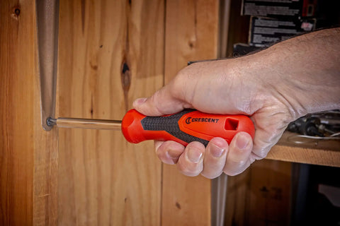 Quarter Inch Drive Dual Material Bit Holding Screwdriver Handle With Ergonomic Balance Grippy Oil And Solvent Resistant Grip Full Polish Chrome Shank Pro Grade Quality Meets ANSI ASME Specs used to tighten a screw on a wooden surface.