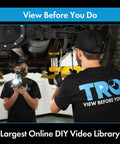 Two mechanics working on car suspension, wearing black TRQ shirts, in an automotive repair shop.