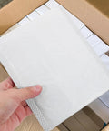 Hand holding a 100 Pack Bubble Envelope Mailers 15x18 Inches Plus 4cm Self Seal Waterproof Packaging Bag, box background