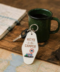 Four Piece Vintage Keychain Set For Camper RVs Retro Black And White Fobs Lightweight Durable Plastic Key Tags For The Fam Organization And Everyday Use shown next to a green mug and maps.