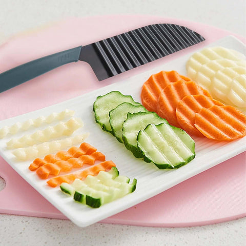 Large crinkle cutter knife with gray handle and black striped blade, beside sliced cucumbers and carrots on a plate.