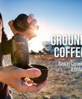 Person using Minipresso GR Portable Espresso Machine For Ground Coffee, manual hand press by the beach, sunlight in background.