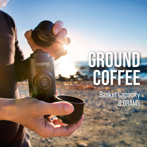 Person using Minipresso GR Portable Espresso Machine For Ground Coffee, manual hand press by the beach, sunlight in background.