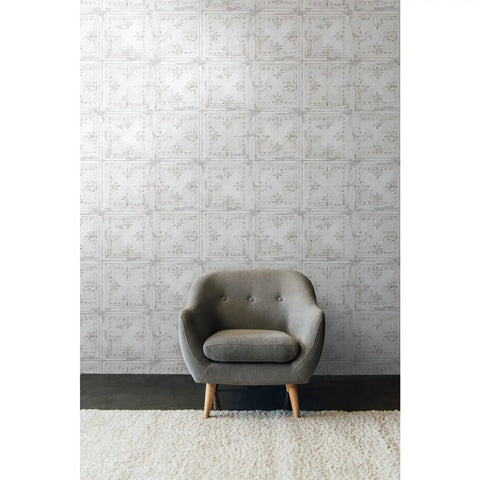 White Tin Tile Metallic Peel And Stick Wallpaper Easy Install DIY Friendly Repositionable And Removable No Mess Accent Wall Decor 20.5 Inch Wide By 16.5 Feet Long Covers About 28.2 Sq Ft used as accent wall behind gray armchair and rug.