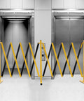 Hardcore Expandable Metal Barricade, Pro Ready Portable Safety Fence With Rock Solid T Base, Zero Hassle Folding Traffic Barrier Gate For Construction Zones And Crowd Control In High Vis Yellow set up in front of elevators.