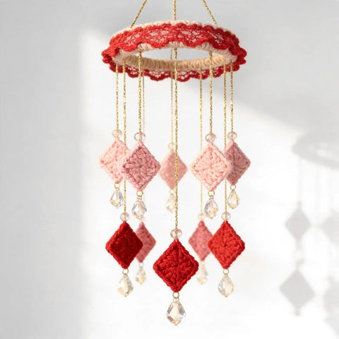 Hanging mobile with red and pink crocheted squares and crystal embellishments on decorative metallic bakers string gold twine.