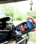 Person pouring Marine Fuel System Treatment 32 Oz For Boats And Watercraft into boat fuel tank, near a dock.