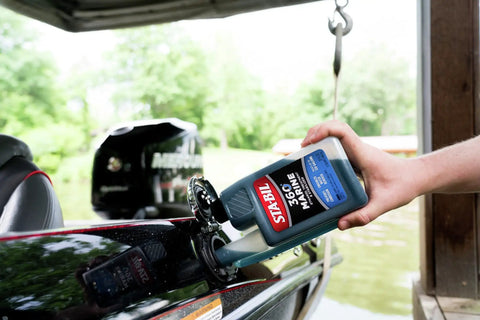 Person pouring Marine Fuel System Treatment 32 Oz For Boats And Watercraft into boat fuel tank, near a dock.