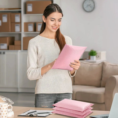 A woman holding a light pink padded envelope for Large Bubble Mailers 12x16 Inch Pack Of 25 No Fuss Usable Inner 12x15 Inch Size