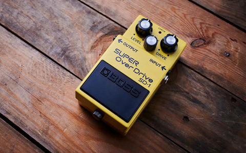 SD1 Super Overdrive Pedal For Electric Guitars With Tube Like Clipping Dynamic Tone Options And Easy To Use Controls For Blues Rockin And Metal A Genre Defining Drive That Stacks With Boost And Distortion placed on wooden surface.