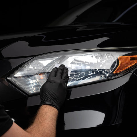 CERAKOTE Ceramic Headlight Restoration Kit being applied to a car headlight by gloved hand on a black vehicle.