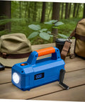Blue portable flashlight with ergonomic orange handle and digital display, placed on a wooden table in a forested environment.
