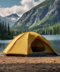 Yellow tent pitched by a mountain lake with forest and mountains in the background under a cloudy sky.
