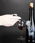 A person wearing disposable latex exam gloves cleaning a wine bottle with a brush and a glass of red wine nearby.