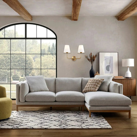 Living room with Two Light Wall Sconce With White Fabric Tapered Shades In Dope Antique Brass Finish above a gray sectional sofa.