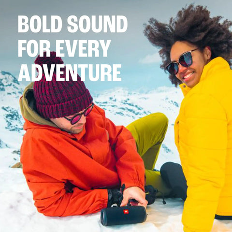 Two people using Flip 5 Dope Waterproof Portable Bluetooth Speaker With 12 Hours Of Playtime in snowy outdoors.
