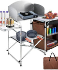 Aluminum Portable Folding Camp Kitchen Table With Windscreen Cupboard And Storage Organizer Carrying Bag For Outdoor Picnics Beach BBQ RV Travel Quick Setup Brown Finish with cookware and storage bag.