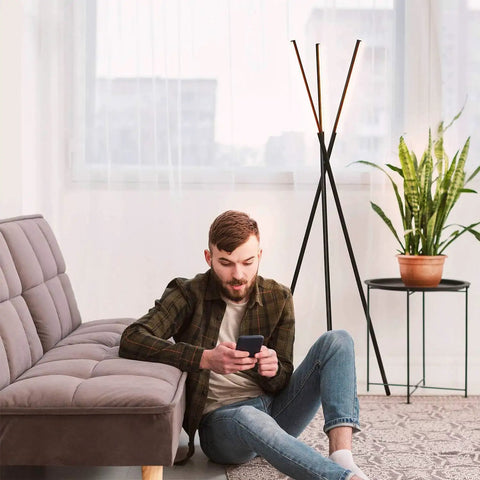 Man sitting near LED Tripod Floor Lamp With Dimmable Lights For Living Room Bedroom And Office Dope Modern Black Standing Lamp With Three Light Heads For Sleek Contemporary Decor.