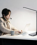Eye Friendly Led Desk Lamp For Home Office With Usb Charging Port Three Level Dimmable Light No Flicker Blue Light Free Compact Reading And Study Table Lamp Black Finish 5000K Cool White in use on a desk next to a man working on a laptop.