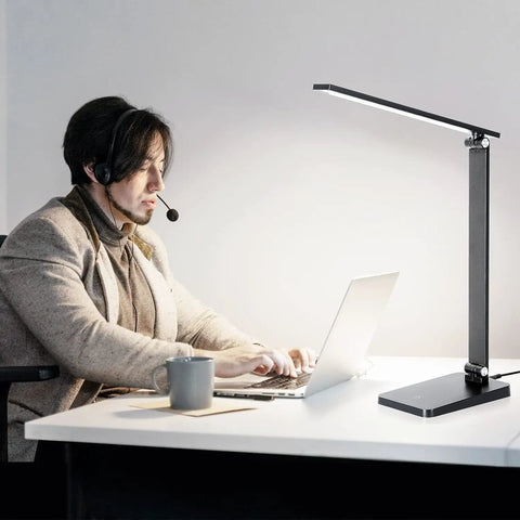 Eye Friendly Led Desk Lamp For Home Office With Usb Charging Port Three Level Dimmable Light No Flicker Blue Light Free Compact Reading And Study Table Lamp Black Finish 5000K Cool White in use on a desk next to a man working on a laptop.
