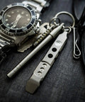 Titanium Ti Pry Mini Pry Bar Keychain EDC Pocket Pry Tool With Bottle Opener next to watch and glasses.