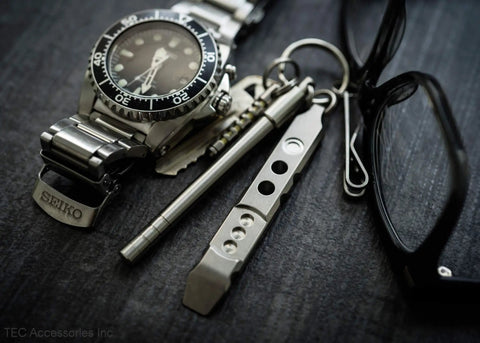 Titanium Ti Pry Mini Pry Bar Keychain EDC Pocket Pry Tool With Bottle Opener next to watch and glasses.