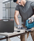 Man using jigsaw on plywood with black carrying case nearby