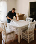 Person wrapping dining table with Two Pack 12 Inch By 72 Foot Nylon Bubble Wrap Roll Heavy Duty Three Sixteenths Inch Perforated Every Twelve Inches For Moving And Shipping Insulation And Cushioning Protection Moisture Resistant Reusable.