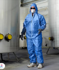 Worker wearing blue disposable coveralls with hood in large size tri laminated SMS polypropylene work suit in industrial setting