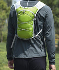 Person wearing Hydration Running Vest Backpack with Water Bladder, green, in outdoor setting, showing adjustable straps and safety strips.