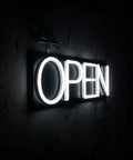 Lit White Neon Open Sign With Remote For Business Front Window Display 20x7 Inch LED Light Up Sign shown from an angle.