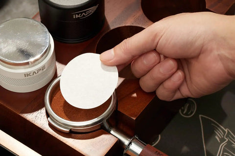 Top Shelf Espresso Barista Gear Featuring 54 Mm Stainless Steel Tamper Fits Breville Portafilters Includes Precision Wdt Needles Sleek Dosing Funnel And Two Hundred Premium Paper Filters To Nail That Perfect Morning Pull, showing a hand placing a paper filter on portafilter.