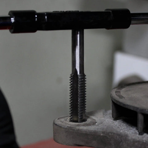 Metric And SAE Tap And Die 60-Piece Rethread Set in use, showing tap cutting internal threads in a metal piece.