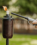 Lighting a honey copper outdoor tiki torch with 2-Pack Honey Copper Outdoor Torches For Patio Backyard And Garden No-Fuss Ready-To-Go Easy-Install Tiki Style Torches With Weather-Resistant Bronze Finish Includes Long-Lasting Wicks And Snuffer Safe And Stylish Ambiance focus keyword