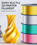 Front view of silk PLA filament spools in gold, silver, teal and pink beside a decorative gold sculpture.