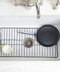 Heavy Duty Kitchen Sink Protector Grid Mat In Black Protects Sink Base From Scratches And Dents Rust Resistant Shield With Elevated Drainage Fits 24 By 12 Inch Sinks XL Size in use with pan and cup