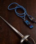 Blue fencing body cord with clamp and epee on wooden surface. Fencing Foil Cord For Epee Mask With Clamp Clear Body Cable Wire Head Clip Portable Training Wire Accessory For Safe Sparring Durable Flexible Electric Foil Cord For Quick Setup And Reliable Contact.