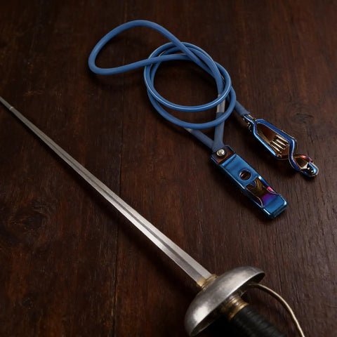 Blue fencing body cord with clamp and epee on wooden surface. Fencing Foil Cord For Epee Mask With Clamp Clear Body Cable Wire Head Clip Portable Training Wire Accessory For Safe Sparring Durable Flexible Electric Foil Cord For Quick Setup And Reliable Contact.