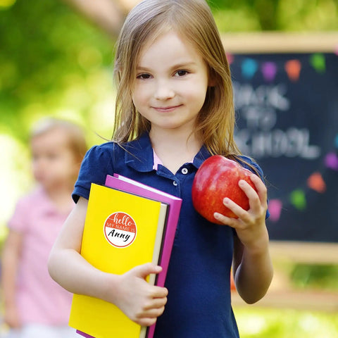 Child holding books and apple with Hello My Name Is Round Name Tag Stickers Set 315 Pcs In 9 Macaron Colors sticker visible
