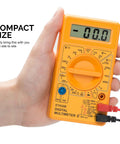 Hand holding orange digital multimeter with LCD display, compact size. Product: Digital Multimeter And Diode And Transistor Tester For Automotive And Home Use Must Have AC DC Volt Meter Battery Tester Analog Multimeter Kit Voltage Meter For Cars And Electronics.