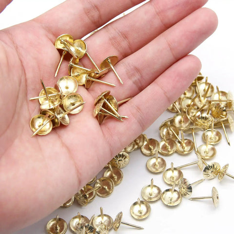 Slick Daisies Antique Gold Upholstery Tacks And 100 Piece Bronze Flat Head Nails With Rust Proof Finish in a hand, showcasing the antique gold color and design.